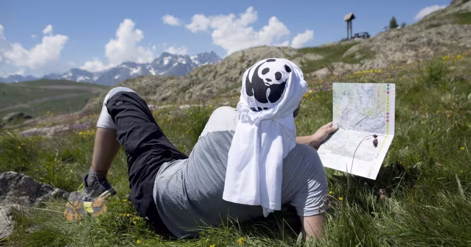 Un pandathlète se repose dans l'herbe en lisant la carte d'orientation du parcours à l'Alpe d'Huez (France)