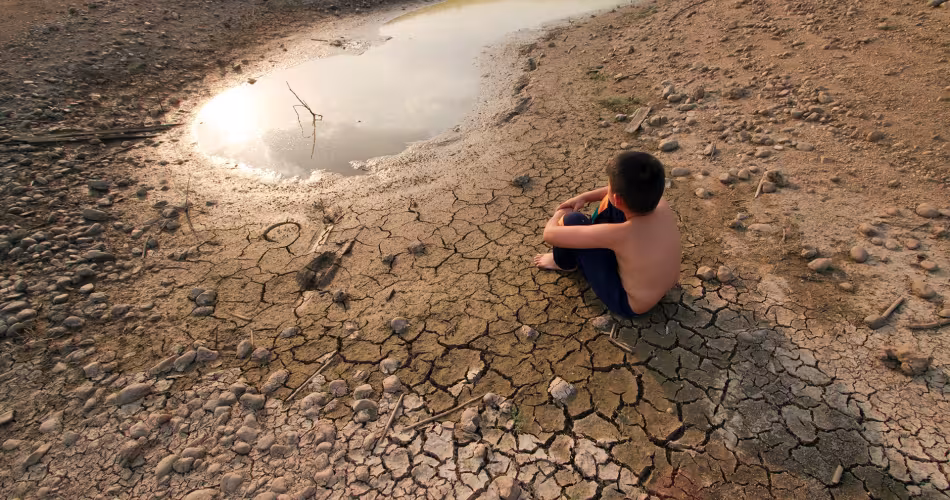 Un enfant est assis au bord d'une mare asséchée